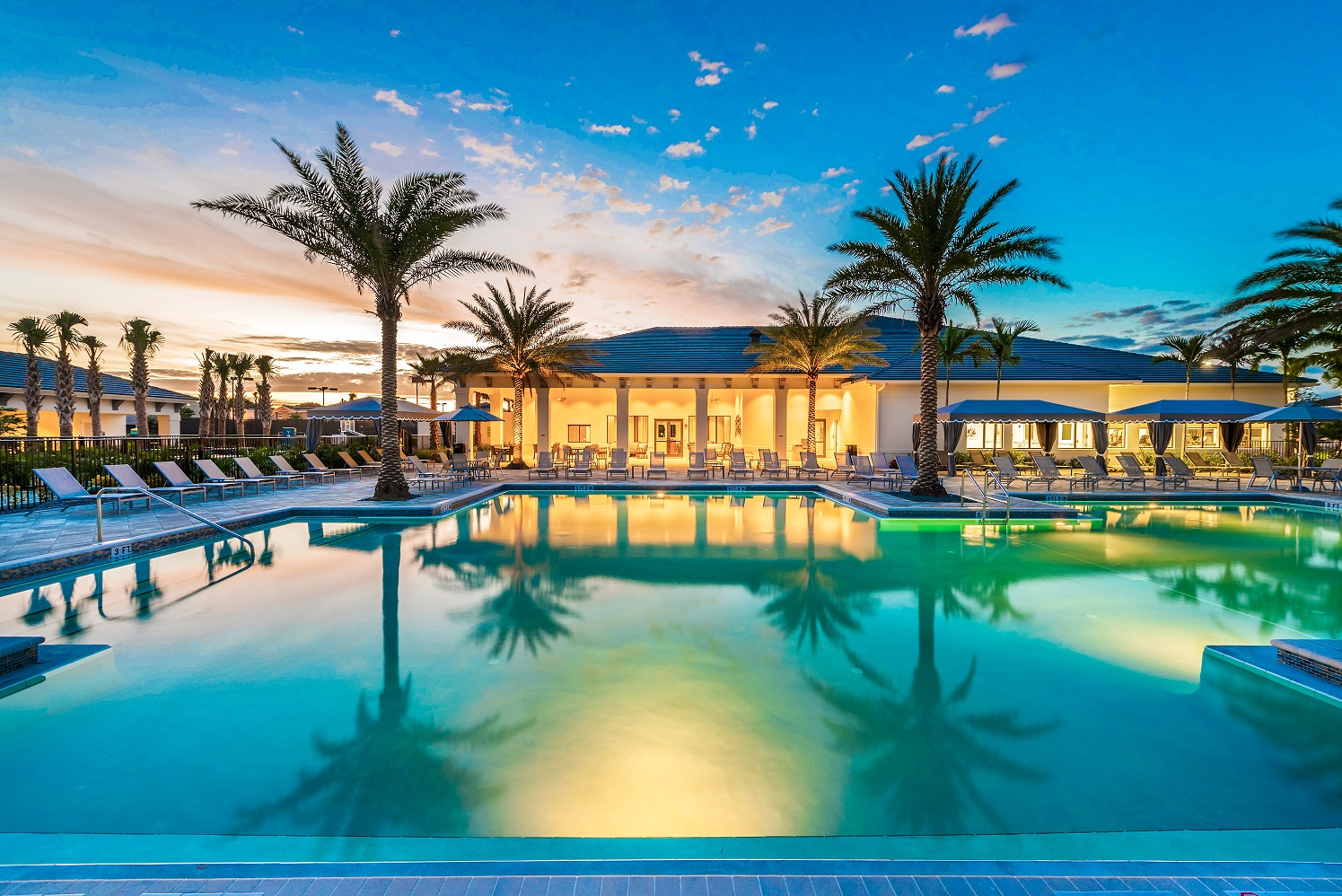 Lagoon-style community pool at sunset, framed by palm trees and the clubhouse